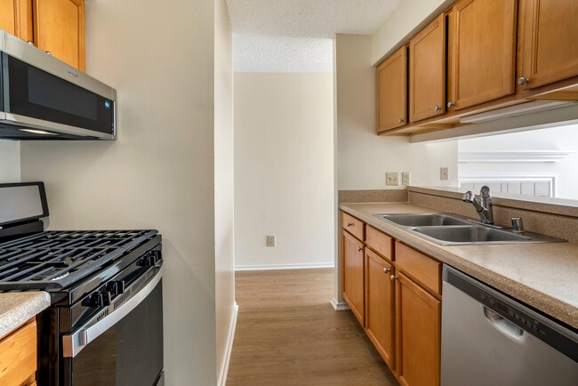 Renovated Package I kitchen with stainless steel appliances, laminate countertops, oak cabinetry, and hard surface flooring - eaves Fair Lakes