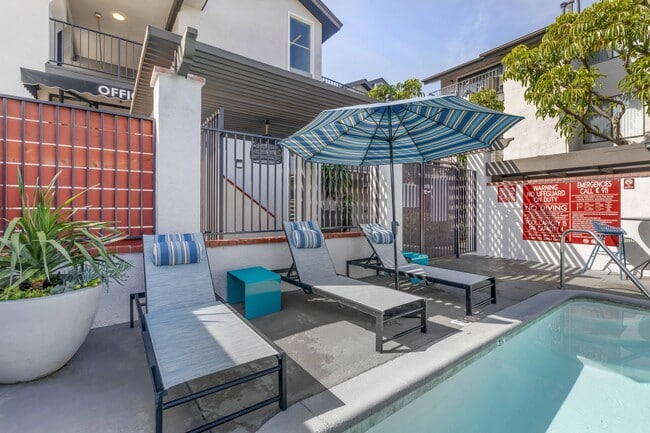 Relaxation meets luxury at Independence Plaza: Your oasis awaits, complete with a serene patio, sparkling pool, and inviting lounge chairs under the shade of a vibrant umbrella. - Independence Plaza Apartment Homes