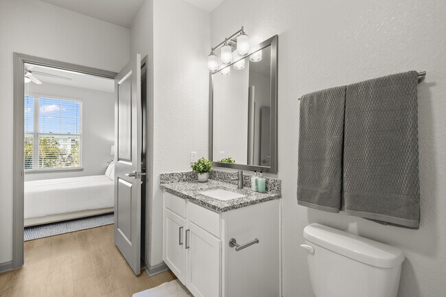 Bright modern bathroom with elegant granite countertop and view into a cozy, sunlit bedroom. - Avana Parkway