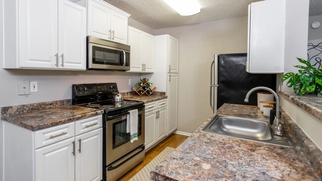 This modern galley-style kitchen features stainless steel appliances, white cabinetry, and expansive countertops—perfect for prepping, cooking, and entertaining. - Grand Oaks At The Lake
