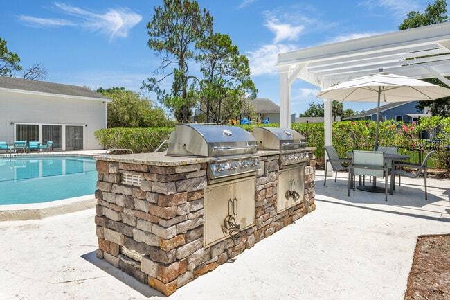 Inviting outdoor space featuring a luxurious poolside area with two sleek stainless steel grills, a stylish pergola, and a cozy patio set, perfect for entertaining. - Vista North