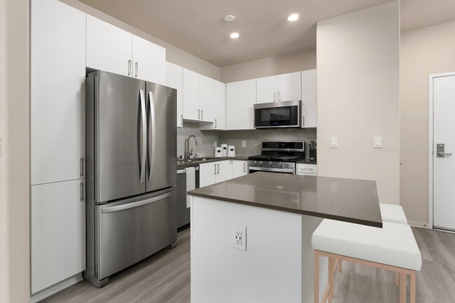 Renovated Package I kitchen with quartz countertops, white cabinetry, stainless steel appliances, hard surface vinyl plank flooring, and tile backsplash - Avalon Playa Vista