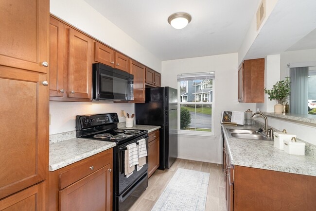 A sleek kitchen featuring stylish black appliances and warm wooden cabinetry for a functional and inviting cooking space. - Windridge Townhomes