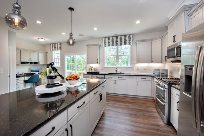 Chef-inspired kitchens featuring stainless steel appliances, granite countertops, and tile backsplash - Avalon Townhomes Brier Creek