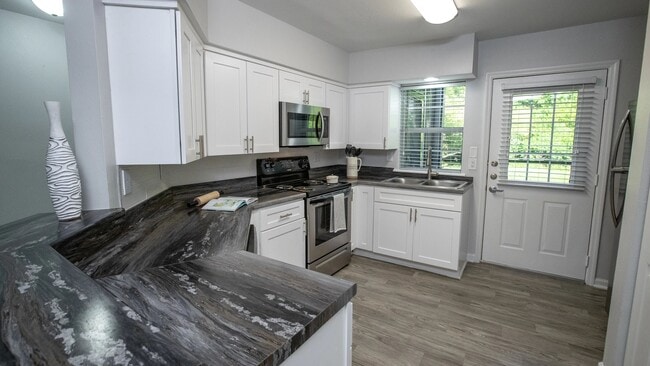 Sleek black fusion countertops, abundant white shaker cabinetry, and stainless-steel appliances create an elegant and functional culinary haven in this spacious kitchen with a breakfast bar. - Emerson Isles