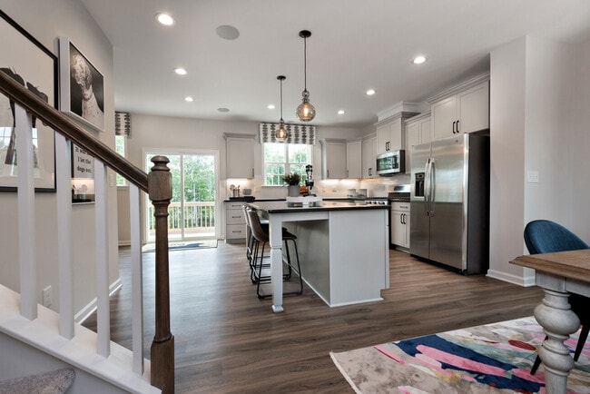Kitchen with light grey cabinetry, black granite countertops, white tile backsplash, stainless steel appliances, and hard-surface vinyl flooring - Avalon Townhomes Brier Creek