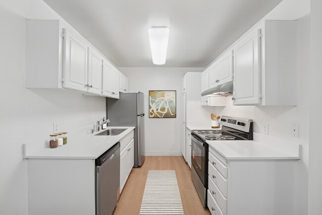 Renovated Package I kitchen with white cabinetry, white quartz countertops, stainless steel appliances, and hard surface flooring - eaves Foster City