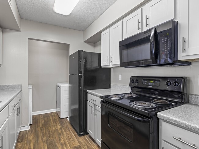 Well-appointed kitchens feature black refrigerator, stove, and white cabinetry, professionally operated by Highlands Vista Group. - Park at Meadow Ridge