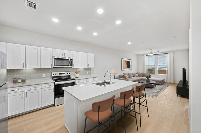 Renovated Package I kitchen with white cabinetry, grey quartz countertops, grey subway tile backsplash, stainless steel appliances, and hard surface flooring - Avalon Denver West